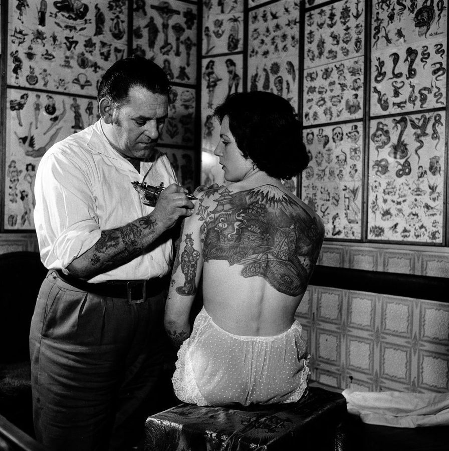 Tatuador tatuando as costas de uma mulher, em um estúdio coberto de flashes